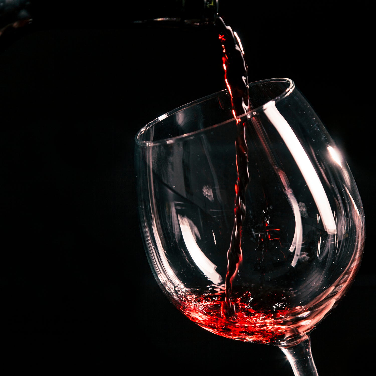Du vin rouge versé dans un verre sur un fond noir.